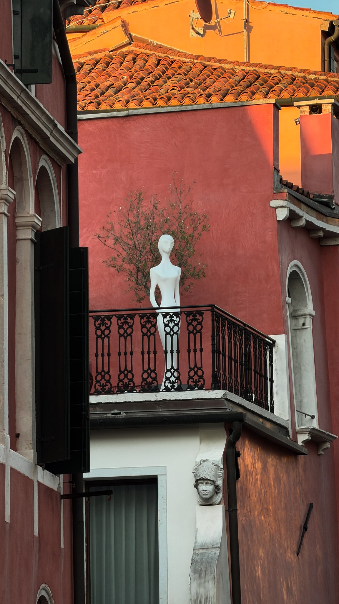 A figure on a balcony, framed by terracotta walls.