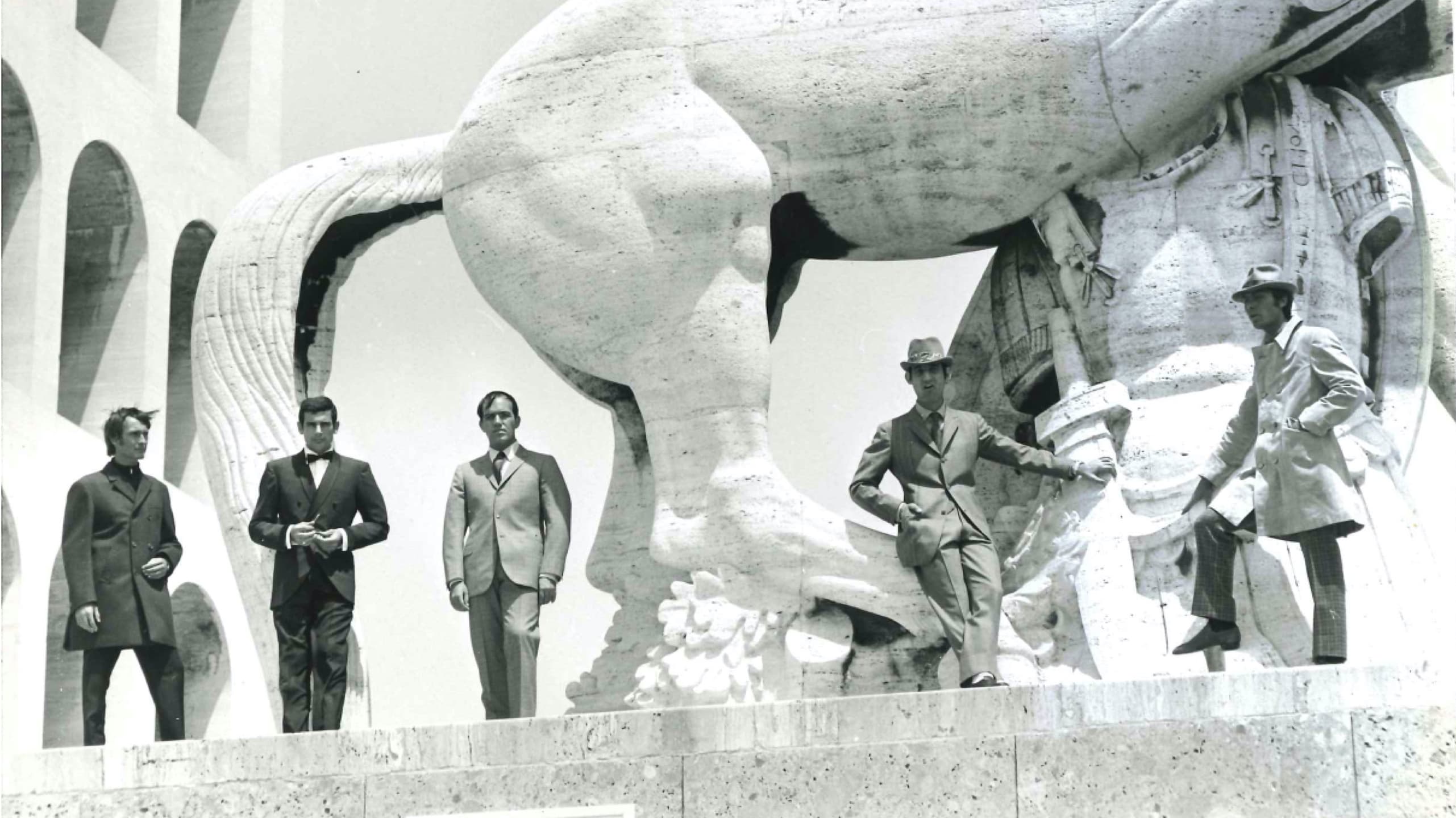Five Brioni models in suits pose by a sculpture in Rome in the 1960s.