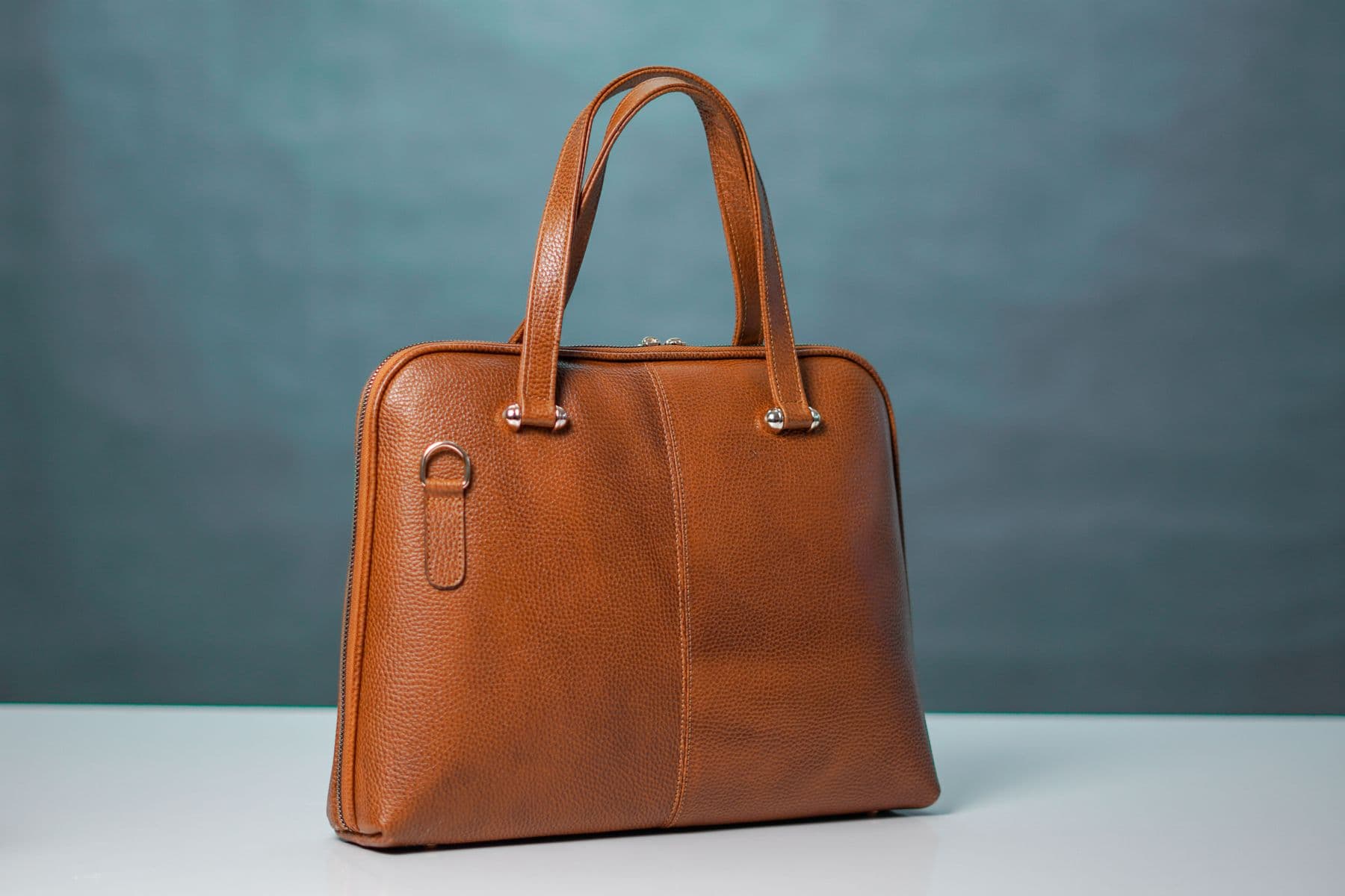 A brown leather handbag standing upright, showing its handles, seams and zipper.