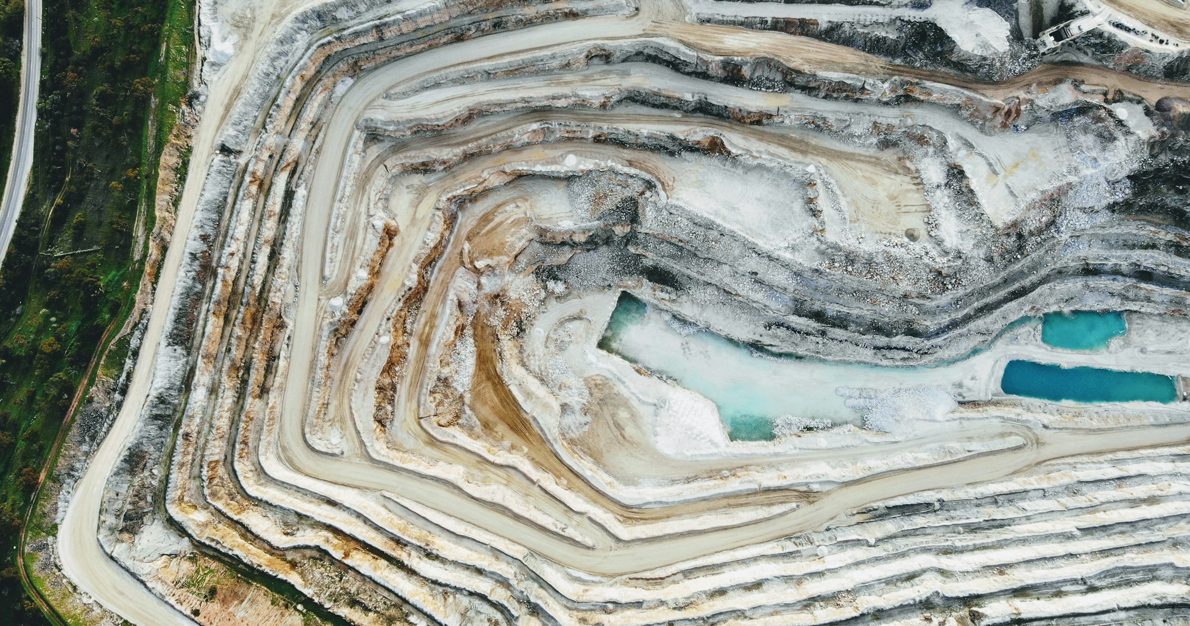 An aerial view of a terraced quarry with pale stone and blue pools.