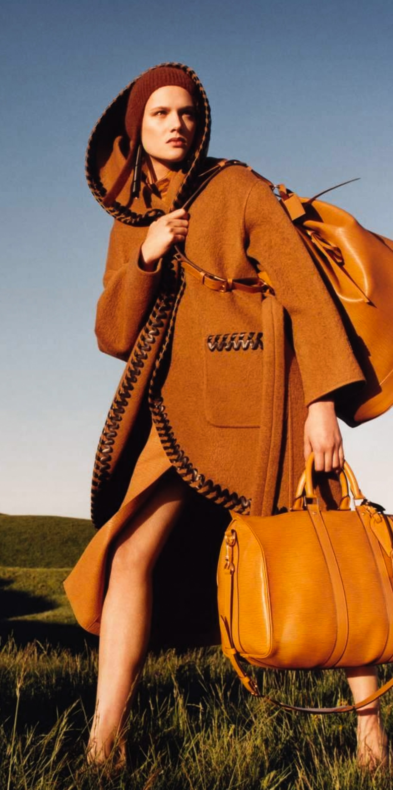 Ochre hooded coat and leather bags against an open blue sky.