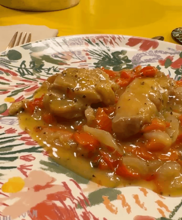 Cooked chicken with peppers and sauce on a patterned plate.