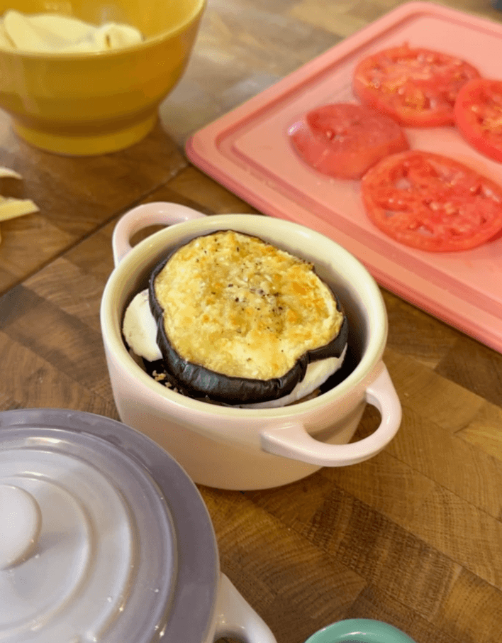 Parmigiana layered in a small pale pink casserole, with tomato slices nearby.